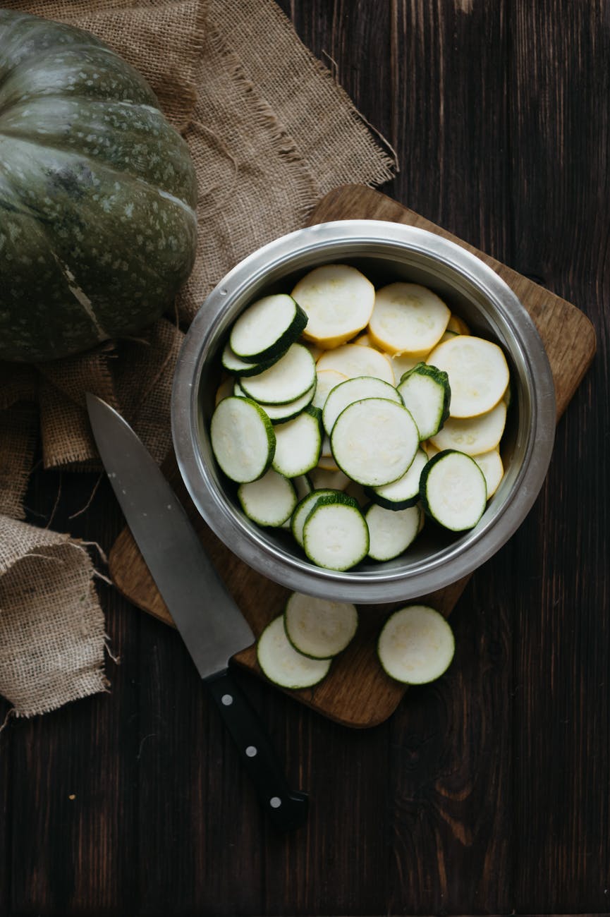 sliced zucchini in a stainless bowl on brown wooden chopping board